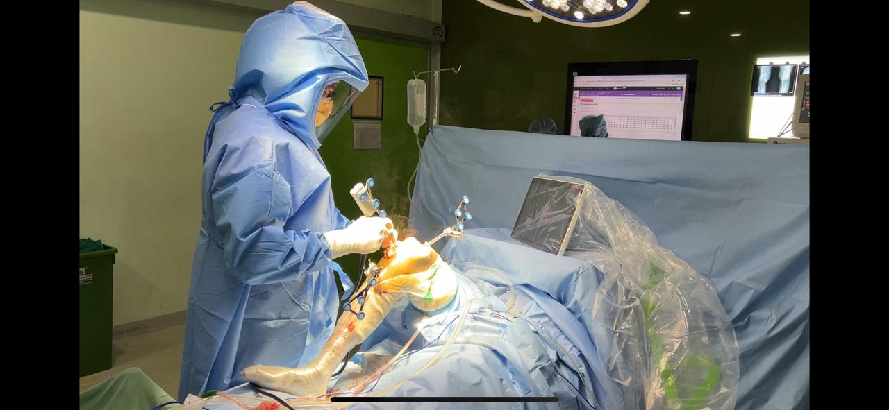 Surgeon operating on a draped joint under theatre lights at NHS Hospital